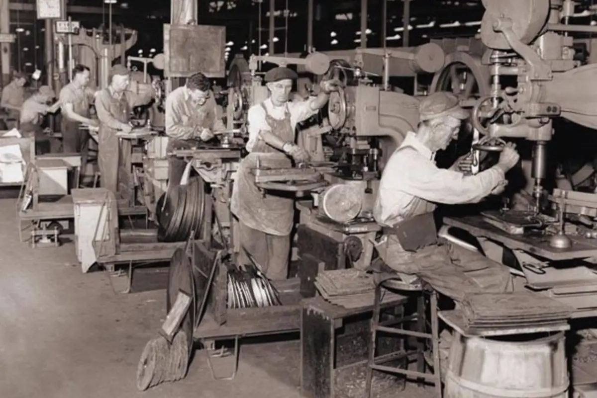 Vue en noir et blanc d'un atelier o&ugrave; 7 hommes s'affairent chacun sur sa machine