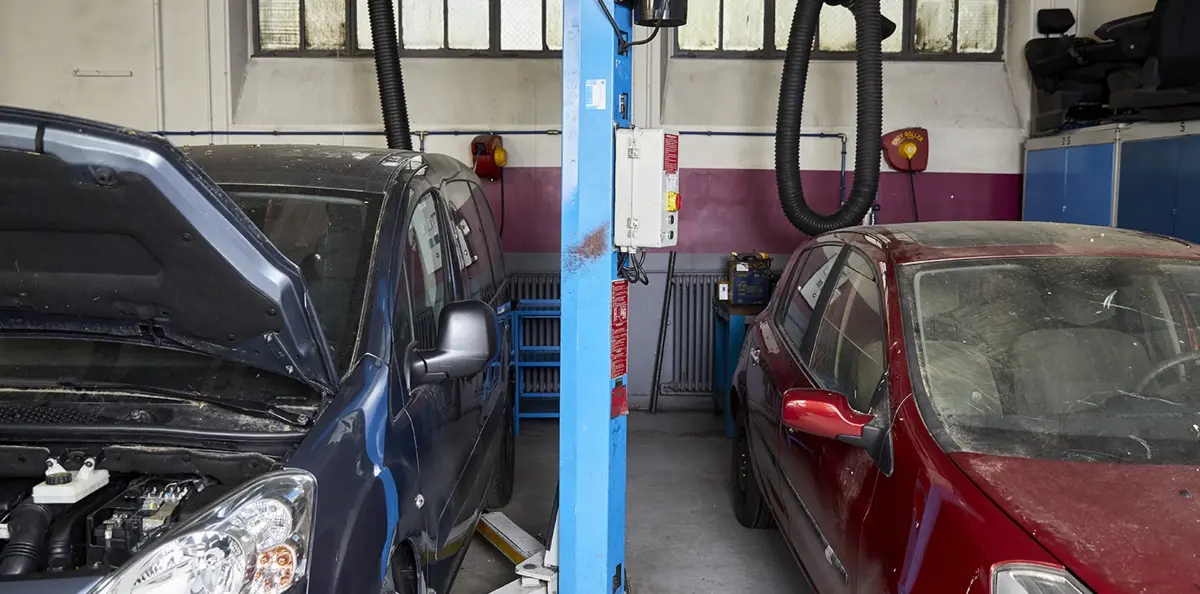 Une voiture bleue capot ouvert et une voiture rouge c&ocirc;t&eacute; &agrave; c&ocirc;te dans un garage automobile