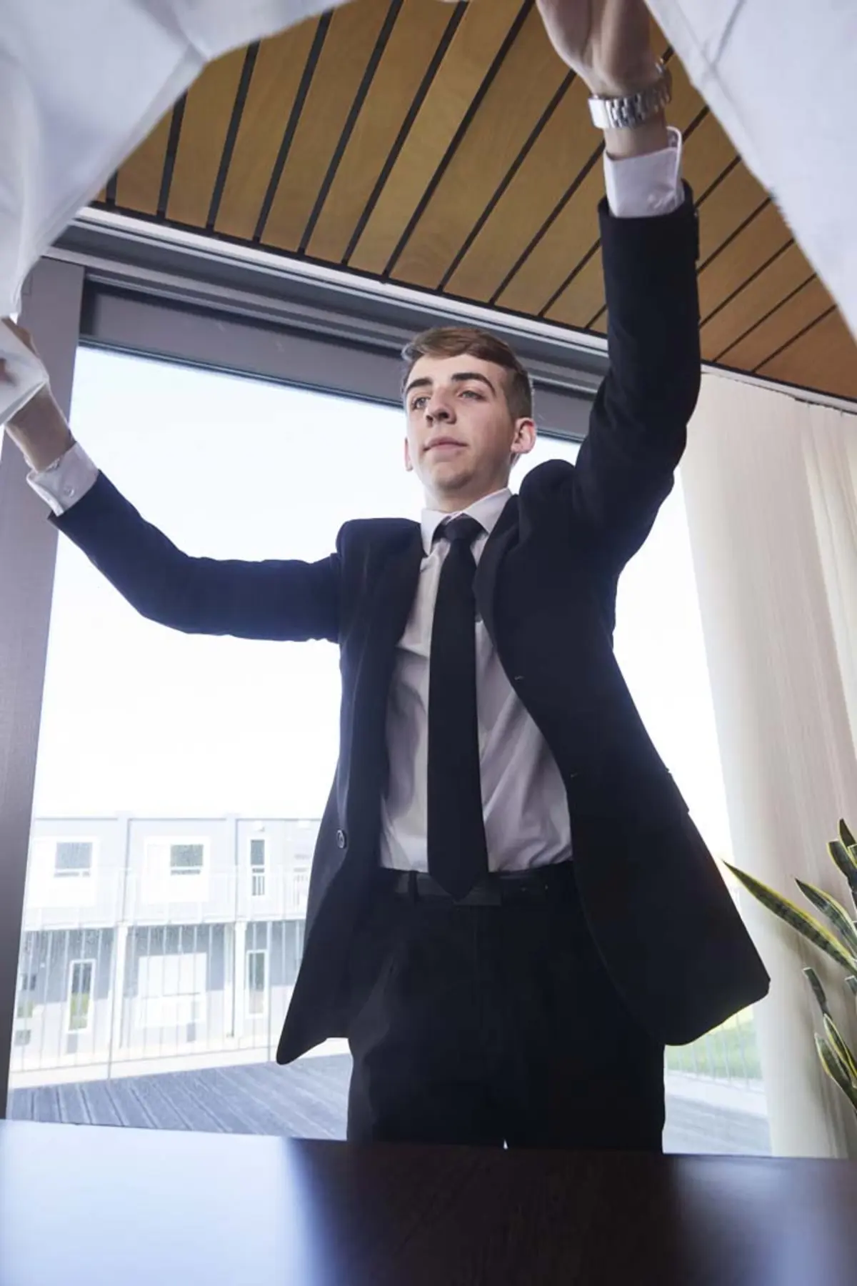 Maxence, en costume cravatte, entrain de poser une nappe sur une table
