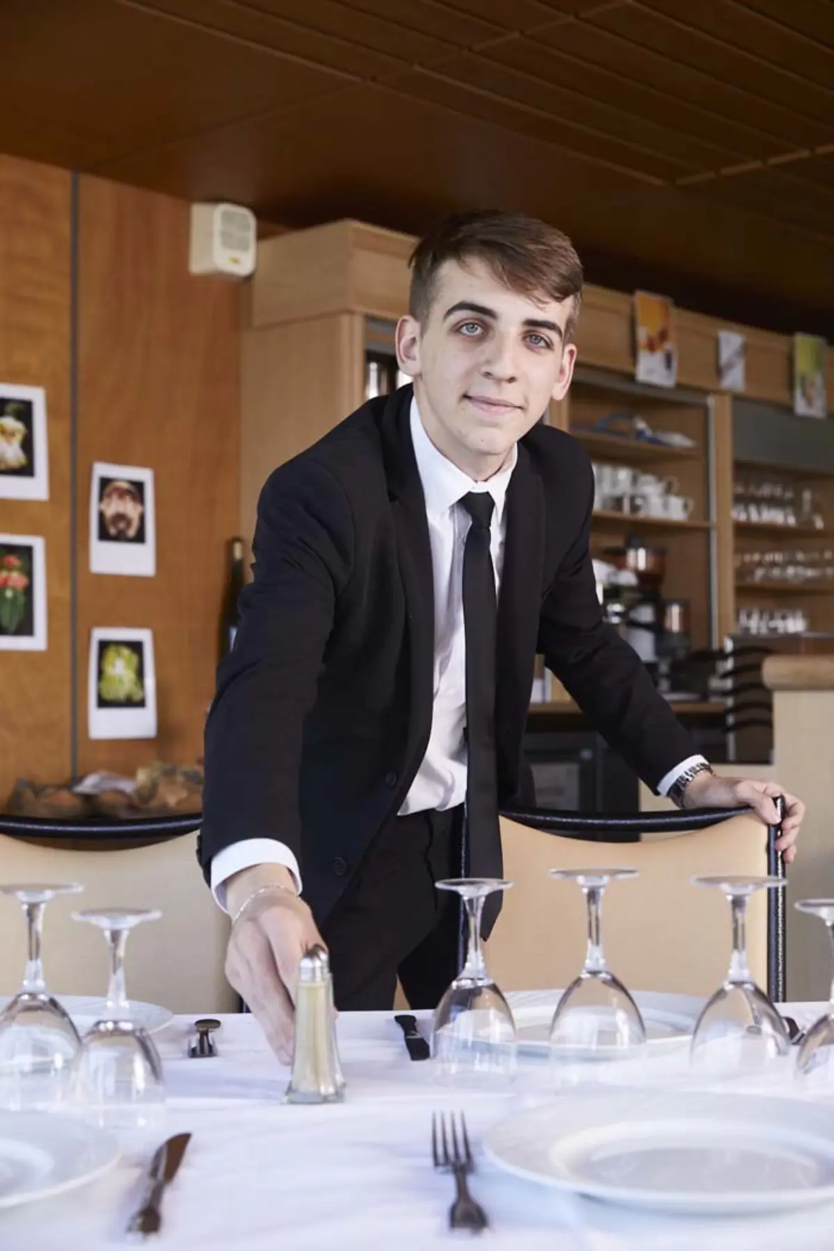 Maxence, en costume cravatte, pose une sali&egrave;re sur une table dress&eacute;e d'assiettes et de verres &agrave; pied