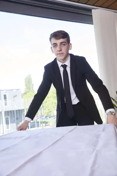Maxence, en costume cravatte, a pos&eacute; une nappe sur une table