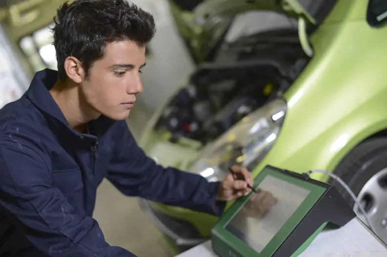Dans un atelier de maintenance automobile, un jeune homme pose devant un tableau de contr&ocirc;le des r&eacute;parations.