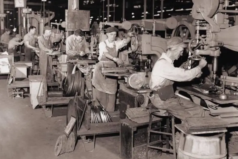 Vue en noir et blanc d'un atelier o&ugrave; 7 hommes s'affairent chacun sur sa machine